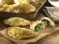 Empanadillas de espinacas y queso recién horneadas, doradas y crujientes, con un relleno cremoso y sabroso.