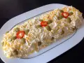 Brazo de gitano de patata cubierto de huevo duro rallado, aceitunas verdes y rodajas de pimiento rojo.