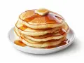 Pila de pancakes dorados con mantequilla y sirope cayendo. ¡Perfectos para tu receta de pancakes!