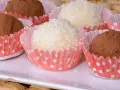 Deliciosas trufas de coco y chocolate, algunas cubiertas de coco rallado y otras de cacao en polvo, presentadas en capacillos rojos con puntos blancos.