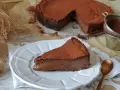 Una rebanada de torta de chocolate, cubierta de cacao en polvo, reposa en un plato blanco. El postre se ve cremoso y delicioso.