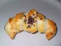 Croissant de chocolate recién horneado, dorado y brillante, espolvoreado con virutas de chocolate.