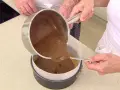 Vertiendo cobertura de chocolate sobre una base de galleta para un delicioso pastel de chocolate.