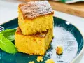 Dos porciones de bizcocho de calabaza, espolvoreadas con azúcar glas, junto a hojas de menta fresca en un plato azul.