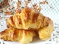 Dos croissants caseros dorados y brillantes, apilados en un plato blanco.