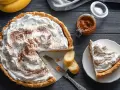 Deliciosa banoffee tarta con abundante nata, espolvoreada con canela. Un trozo ya servido y plátanos frescos acompañan.