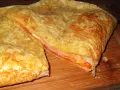 Empanada de jamón y queso dorada, con queso gratinado y relleno jugoso. ¡Un bocado delicioso!