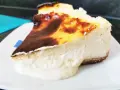 Porción de chese cake con borde quemado y relleno cremoso, servida en plato blanco.