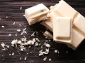 Deliciosos postres con chocolate blanco, trozos y virutas esparcidos sobre una tabla de madera oscura.