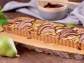 Tarta rectangular con peras y chocolate, decorada con menta. Una pera fresca reposa a un lado.