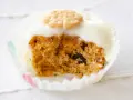 Un muffin de zanahoria con glaseado blanco y una galleta decorativa en forma de flor.
