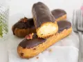 Pastel eclair cubierto de chocolate, relleno de crema. Decorado con pétalos secos.