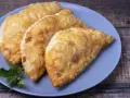 Tres empanadas doradas y crujientes, perfectas para tus recetas con obleas de empanadillas. Decoradas con perejil fresco.