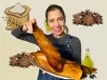 Mujer sonriente muestra una coca de vidre dorada, con ingredientes como harina, anís y aceite de oliva de fondo.