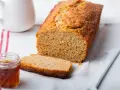 Un delicioso bizcocho con harina integral, recién horneado, con una rebanada cortada y un tarro de miel al lado.