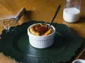 Un esponjoso soufflé con salsa de tomate, listo para disfrutar. Al lado, un batidor y un vaso de leche, ingredientes clave para crear que es un soufflé.
