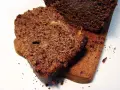 Rebanadas de pan de chocolate húmedo y denso, con trozos de fruta confitada, servidas en una tabla de madera.