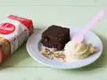 Un delicioso brownie sin huevo con helado de vainilla y nueces, junto a un paquete de Yolanda.