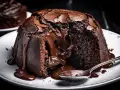 Un delicioso souffle de chocolate con centro líquido, chorreando sobre un plato blanco con una cuchara.