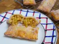Empanada de manzana recién hecha, dorada y espolvoreada con azúcar. Una está partida, mostrando el relleno jugoso de manzana.