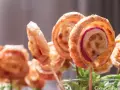Deliciosas piruletas de hojaldre rellenas de queso y jamón, presentadas en un vaso con hojas verdes.