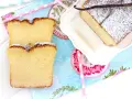 Dos rebanadas de bizcocho de leche condensada, espolvoreadas con azúcar glas, junto a un trozo en un plato con vainilla.