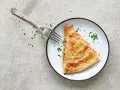 Una porción dorada de empanada de atún, lista para ser disfrutada con un tenedor plateado y espolvoreada con perejil fresco.