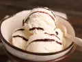 Cuatro bolas de helado de chocolate blanco con sirope de chocolate en un cuenco.