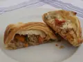 Hojaldre con carne picada y verduras, cortado por la mitad, mostrando el relleno jugoso.