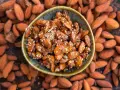 Un cuenco lleno de almendras caramelizadas, cubiertas de semillas de sésamo, rodeadas de almendras enteras.