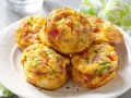 Montón de muffins saludables con huevo, pimiento rojo, cebolleta y jamón, espolvoreados con perejil.