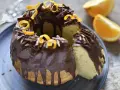 Bizcocho de chocolate y naranja, cubierto con glaseado de chocolate, virutas de chocolate y cáscara de naranja.