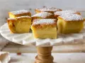 Porciones de un pastel mágico, cubiertas con azúcar glas, sobre un soporte de mármol.