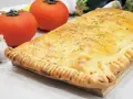 Empanada de pisto dorada y crujiente, con tomates frescos y ajo al lado. ¡Un manjar casero!