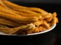 Montón de churros de patata dorados y crujientes apilados en un plato blanco.