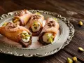 Cuatro cannoli siciliano, crujientes y rellenos de crema dulce, espolvoreados con pistachos y virutas de chocolate.