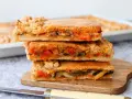 Tres porciones de empanada de verduras apiladas, mostrando el relleno de pimientos, calabacín y tomate.