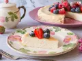 Deliciosa tarta de requesón, decorada con fresas y arándanos, servida en un plato floral.