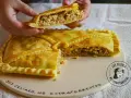 Una mano levanta un trozo de empanada de carne dorada y rellena. La masa crujiente envuelve un sabroso guiso.