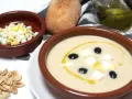Un cuenco de mazamorra cordobesa con aceitunas, huevo duro y un chorrito de aceite. Acompaña un panecillo y almendras.