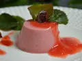 Delicioso panna cotta de fresa, bañado en salsa de fresa y decorado con hojas verdes.