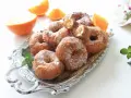 Rosquillas de naranja recién hechas, espolvoreadas con azúcar, junto a gajos de naranja fresca en una bandeja plateada.