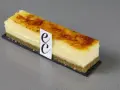 Un trozo de cheesecake creme brulee con base crujiente y cubierta caramelizada, adornado con un distintivo.