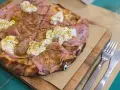 Pizza con mortadela y burrata cremosa, espolvoreada con hierbas verdes y servida en tabla de madera.