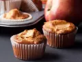 Dos deliciosos muffins de manzana recién horneados, con una manzana roja al fondo.