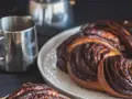 Deliciosa trenza de chocolate recién horneada, humeante junto a una taza de café.