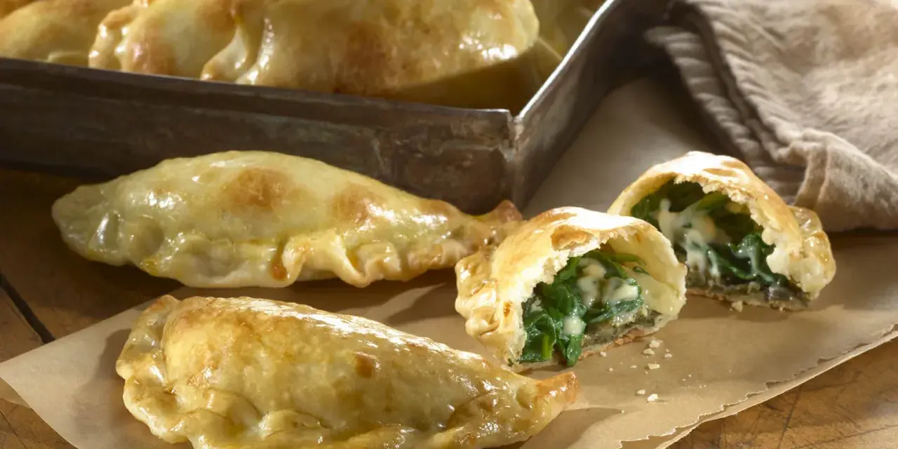 Empanadillas de espinacas y queso recién horneadas, doradas y crujientes, con un relleno cremoso y sabroso.