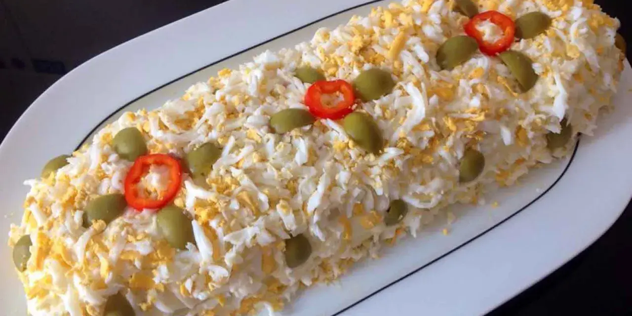 Brazo de gitano de patata cubierto de huevo duro rallado, aceitunas verdes y rodajas de pimiento rojo.