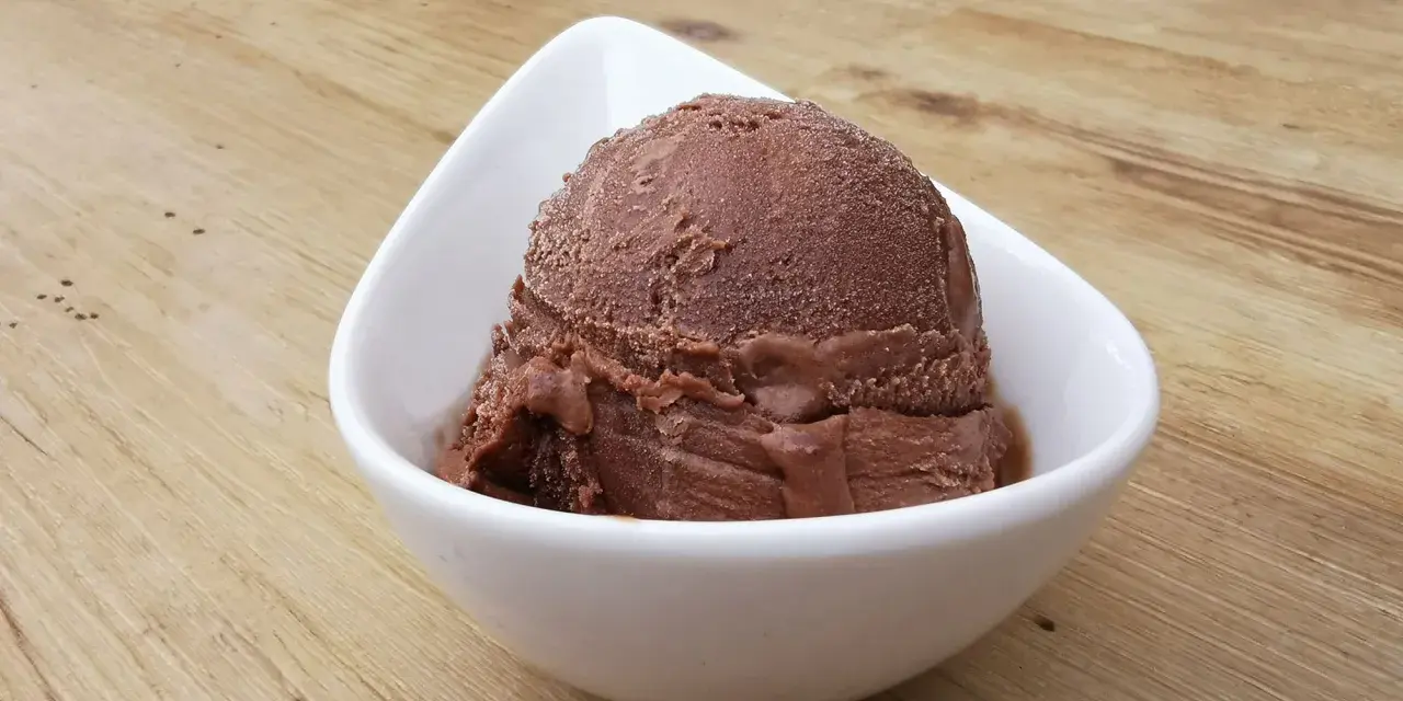 Cremoso helado de platano y chocolate en un cuenco blanco sobre una mesa de madera.