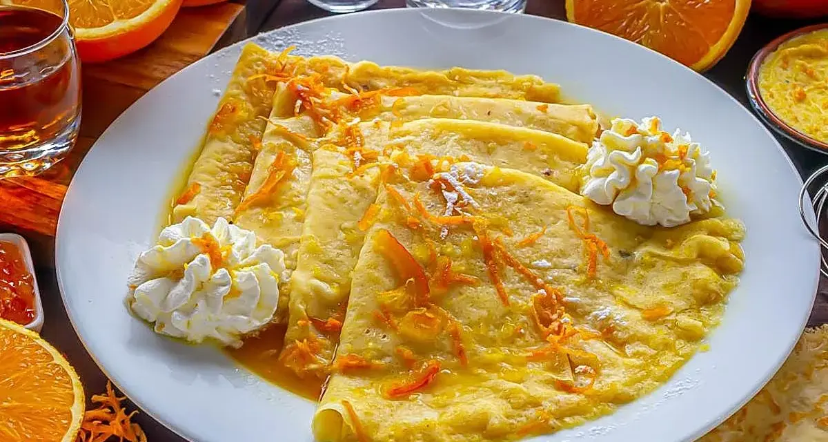 Crepes Suzette, cubiertos con ralladura de naranja y servidos con crema batida.
